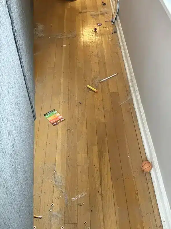 Hardwood floor along a wall scattered with debris before deep cleaning