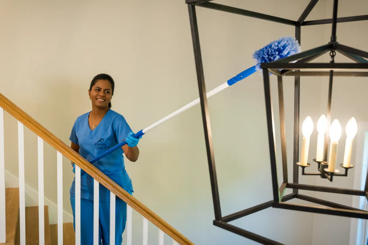 A Family Cleaners team member on a staircase dusting a hanging lantern light with an extendable duster