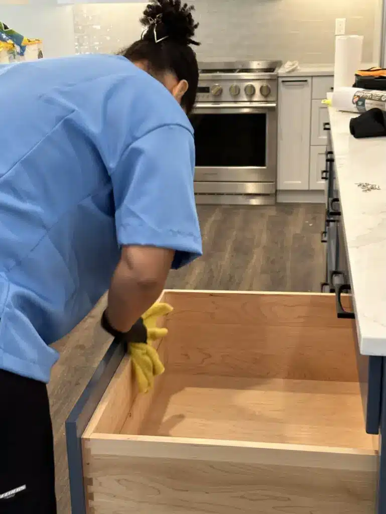 A Family Cleaners team member in gloves wiping the inside of an empty kitchen drawer