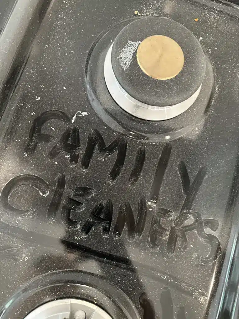 The words Family Cleaners traced in a thick layer of construction dust on a dark surface