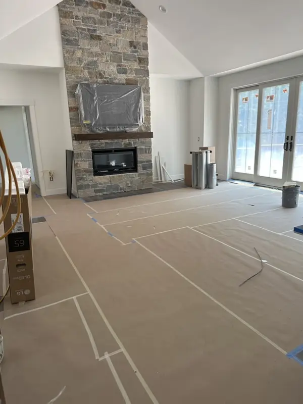 New living room with a stone fireplace, the floor still covered in protective paper
