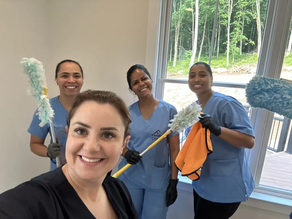Four Family Cleaners team members with extendable dusters, smiling, inside a newly built home