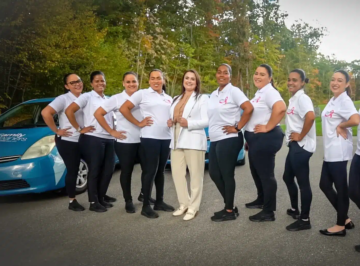 The Family Cleaners team in white company shirts standing in a line with CEO Caroline Compiani, next to a branded company car