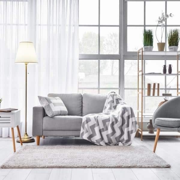 A clean living room with tall windows, a gray couch and a chevron throw blanket.